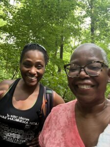 Two brown skinned women with trees behind them.