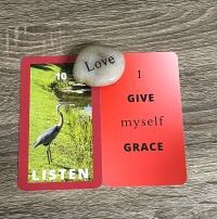 Two 3 x 5 red card with the word Love engraved on a rock between them. Card 1: text Listen with an image of a great blue heron on grass near water. Card 2: text: I give myself grace